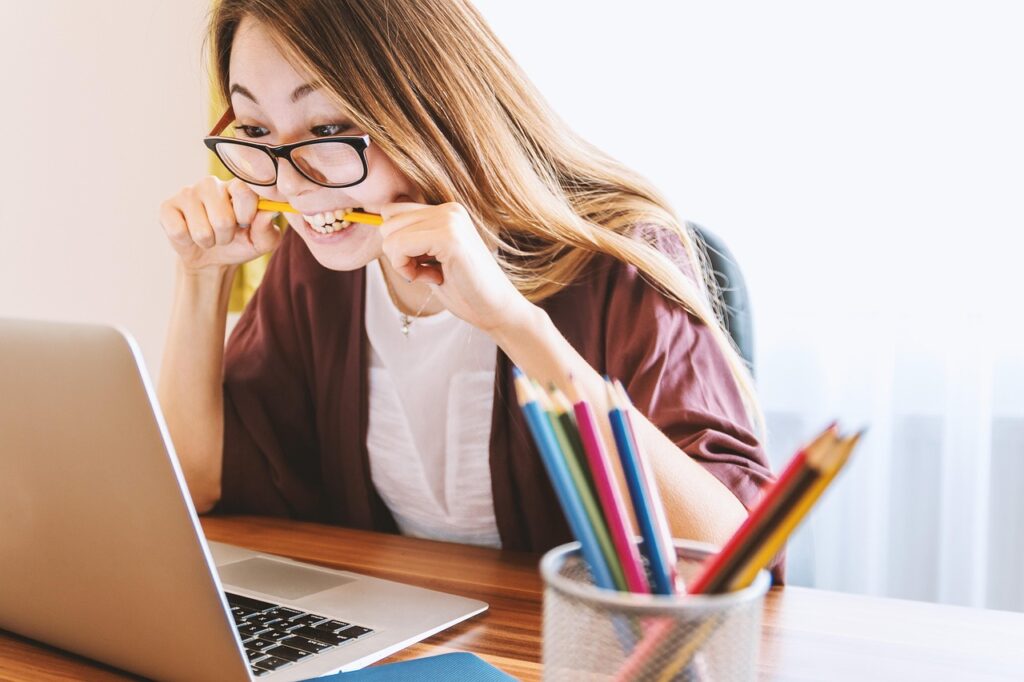  A girl using white laptop and biting a pen 