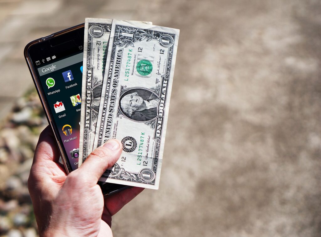 Make money with phone A mobile phone screen and dollar cash are showing in a person's hand.