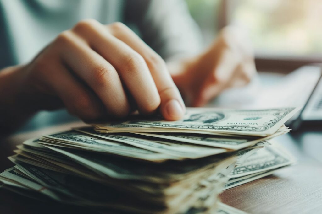 Hands counting a stack of US dollar bills on a wooden table. 