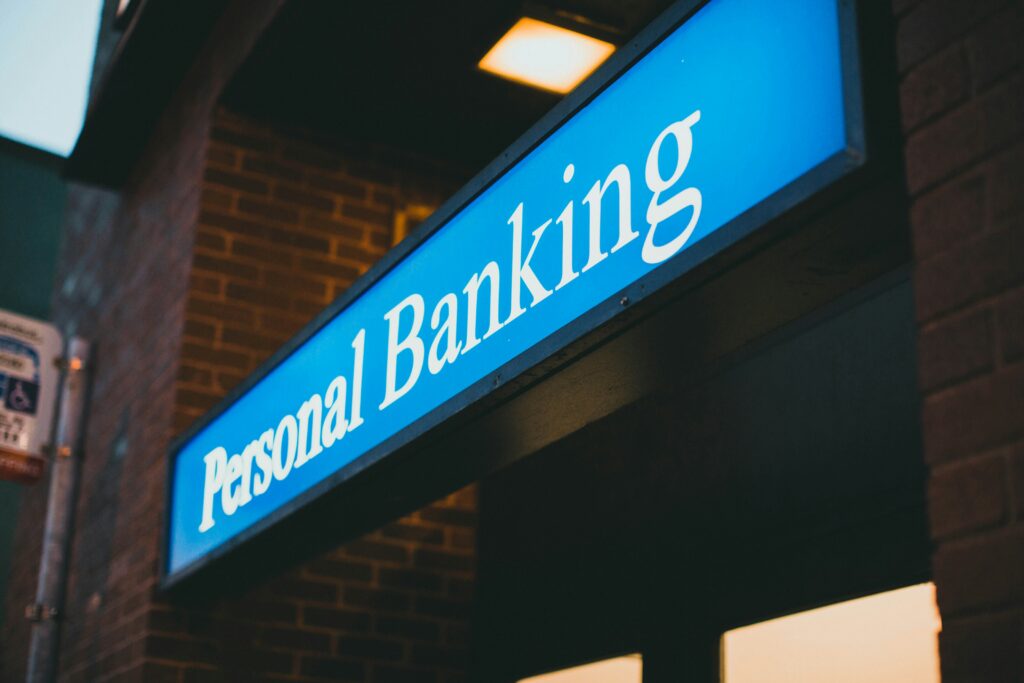 Bright blue sign with white text reads "Personal Banking" on a brick building. The lighting suggests evening, creating a warm, inviting atmosphere.